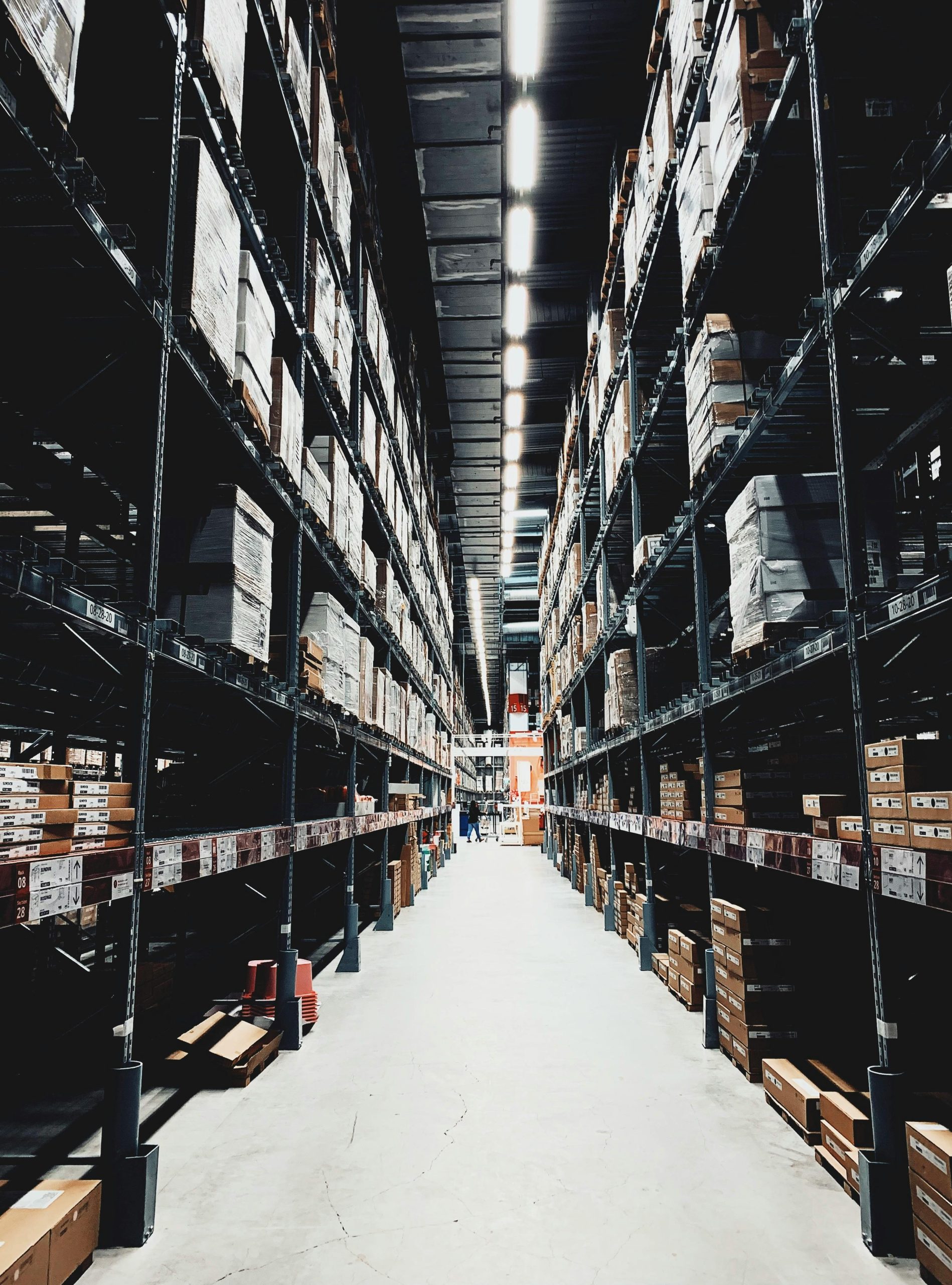 A wide aisle in a large warehouse filled with stacked boxes on high shelves.